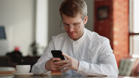 Mann-In-Weißem-Hemd-Und-Modischer-Brille-Ruht-Sich-In-Der-Pause-Im-Café-Aus-Und-Surft-Per-Smartphone-Im-Internet